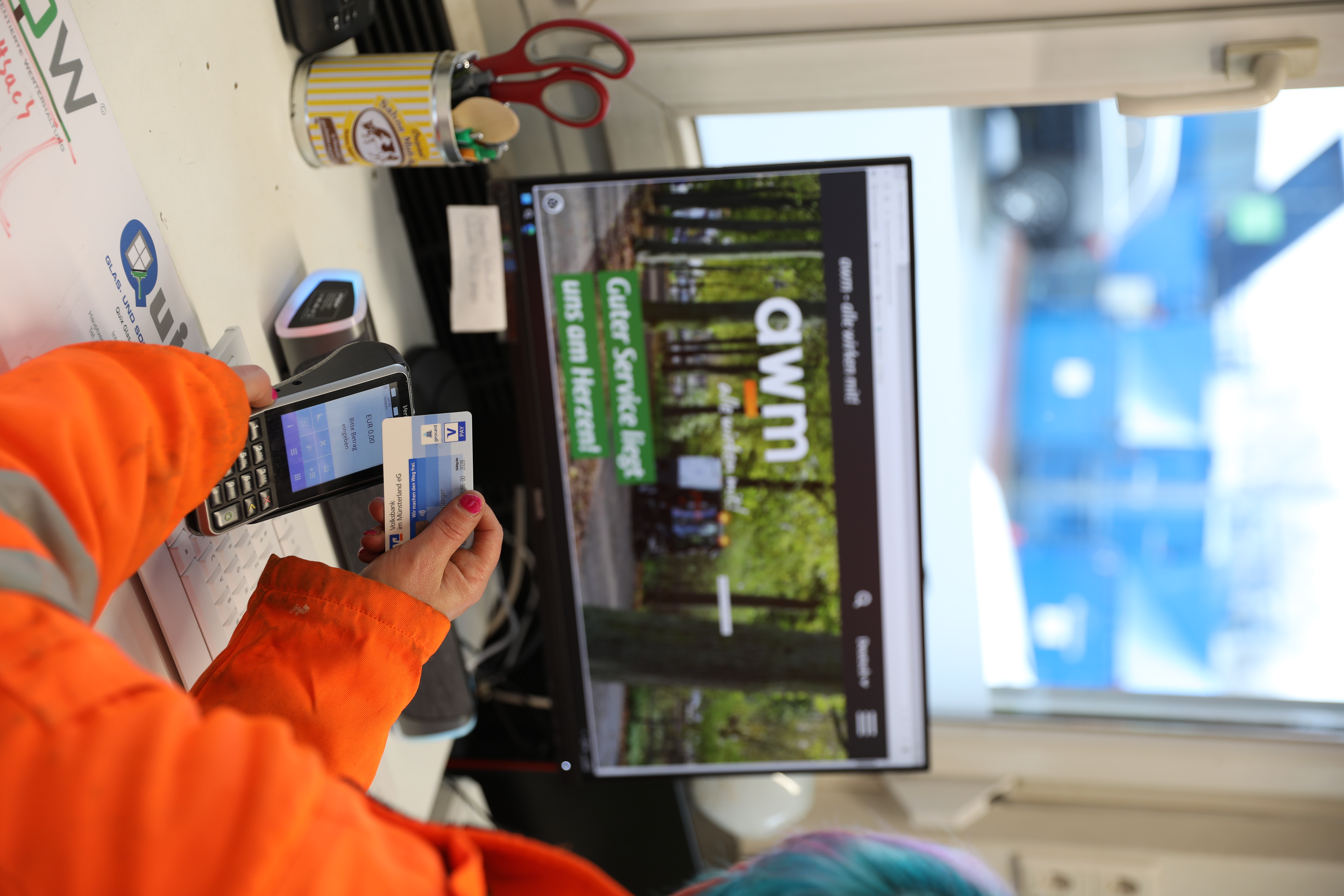 An einem Schreibtisch im Büro oder Kassenhäuschen eines Recyclinghofs wird mit Karte gezahlt.